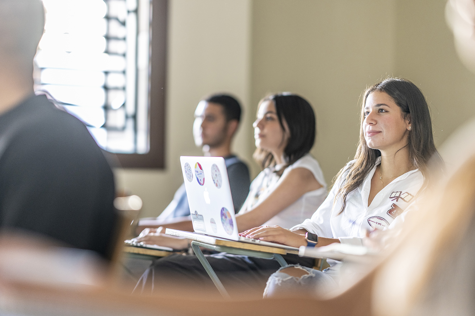 A girl sitting on a desk in class with an open laptop in front of her