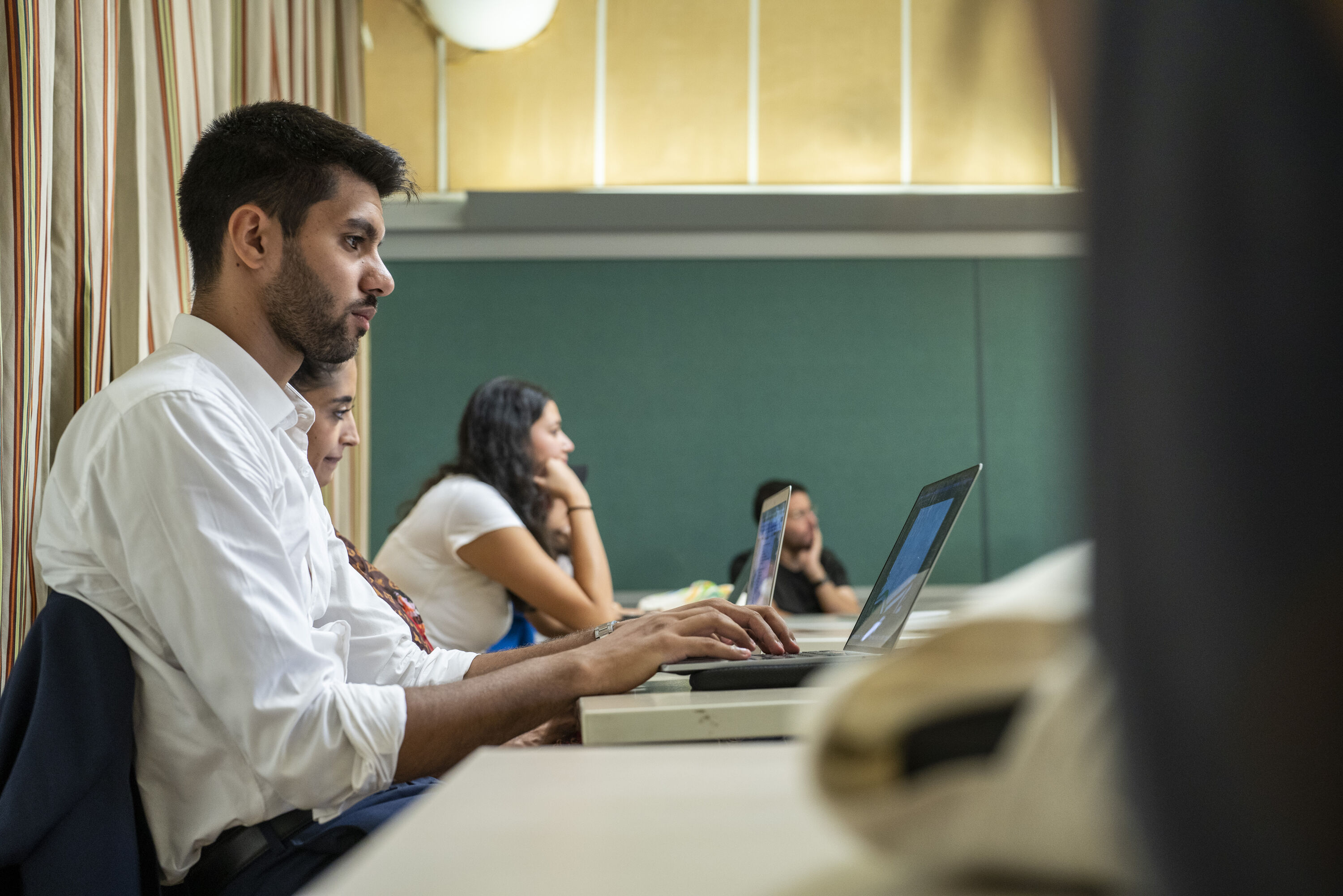 students in a classroom with focus on male student typing notes in class