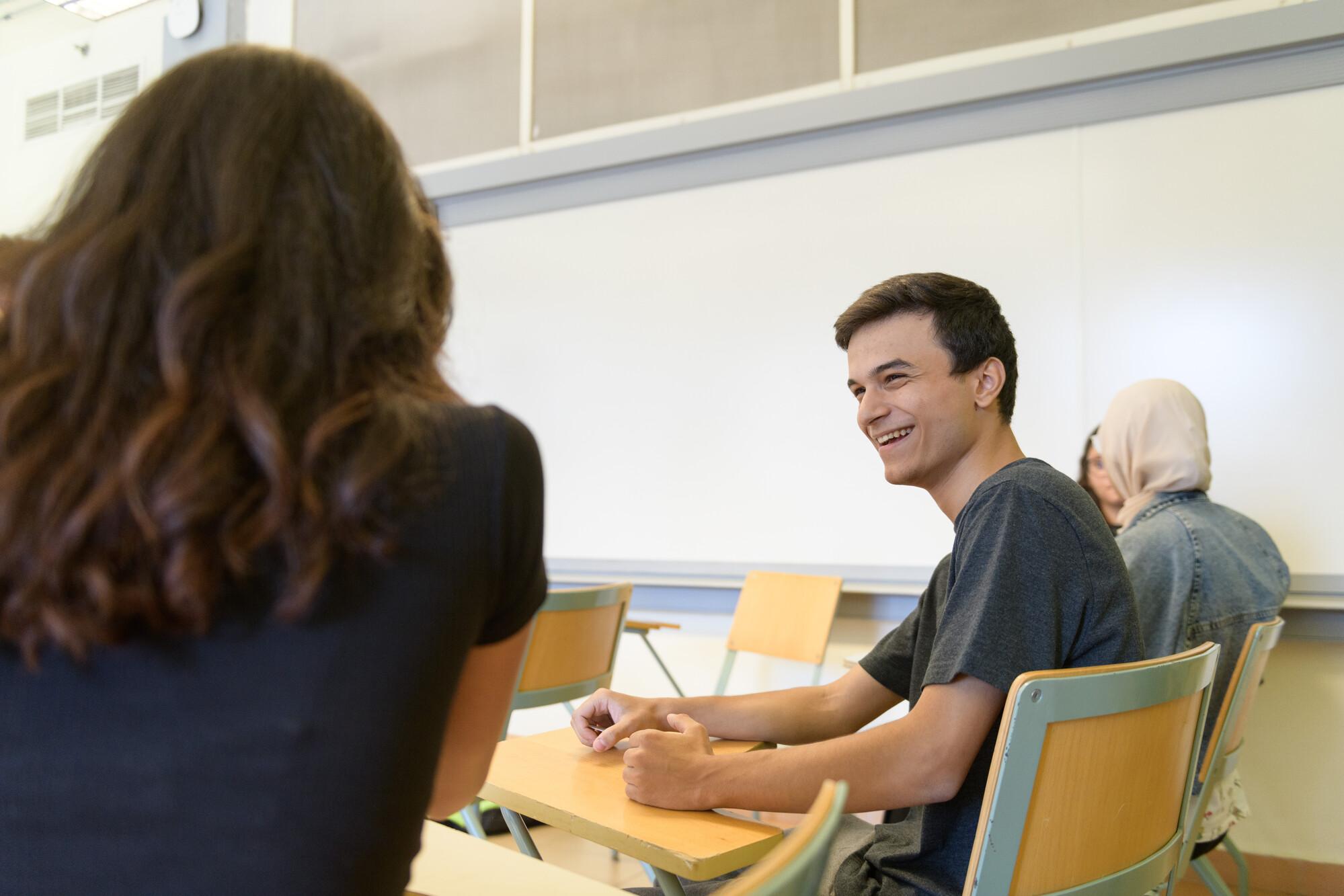 male student smiling and working with a partner in class on a topic