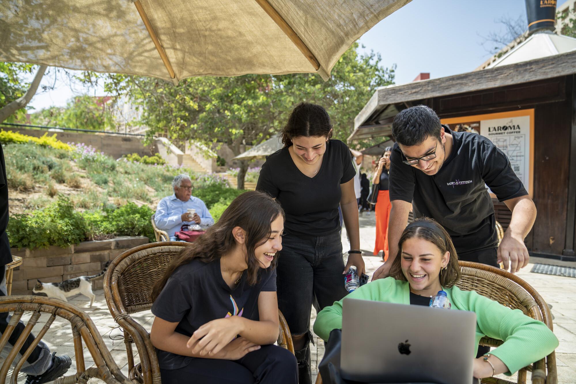 students working in garden on laptop on project and smiling