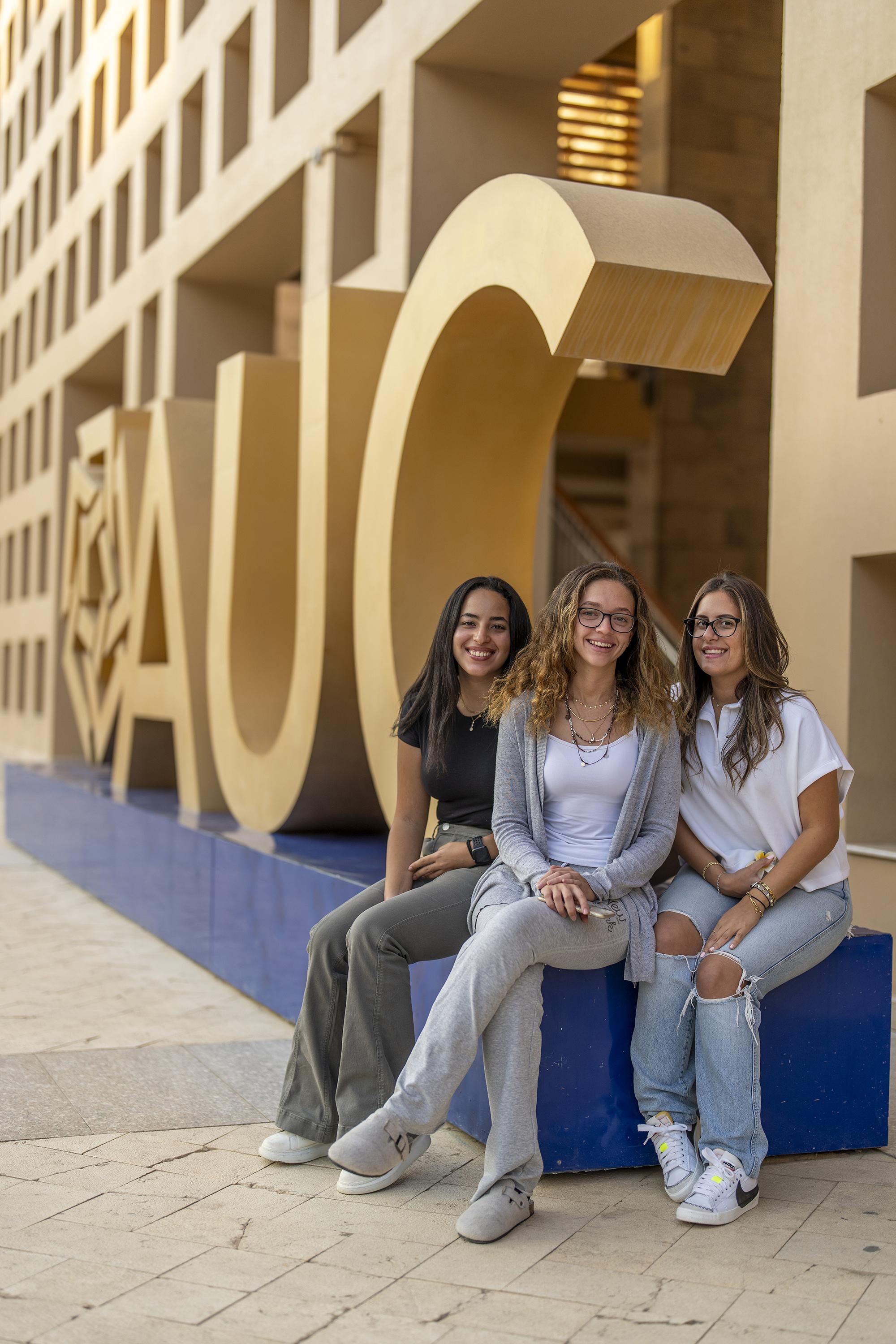 students sitting next to the library next to the AUC logo