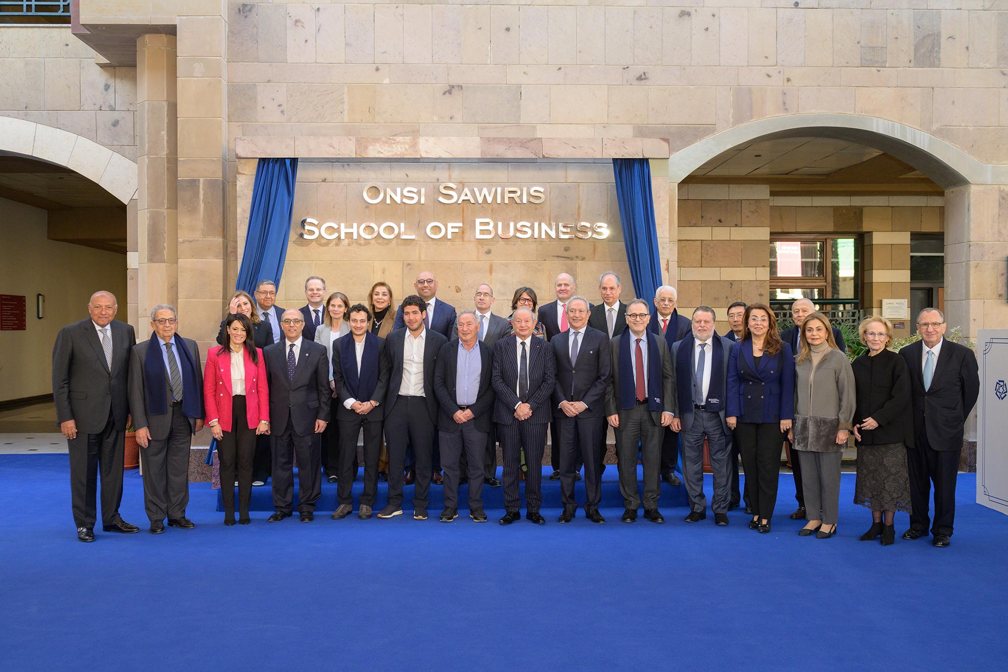 Members of the Sawiris family, senior AUC leadership, ministers, ambassadors and other notable figures standing in front of the Onsi Sawiris School of Business at AUC