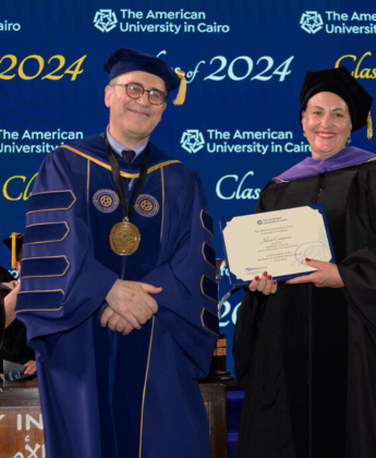 A professor in a cap and a gown holds a certificate next to the President of AUC.