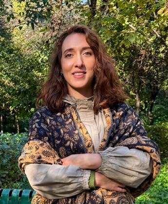 Anastasia stands in a shawl with her arms crossed, outdoors