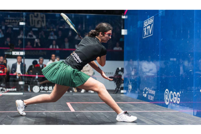 Amina Orfi attacks a squash ball with her racket