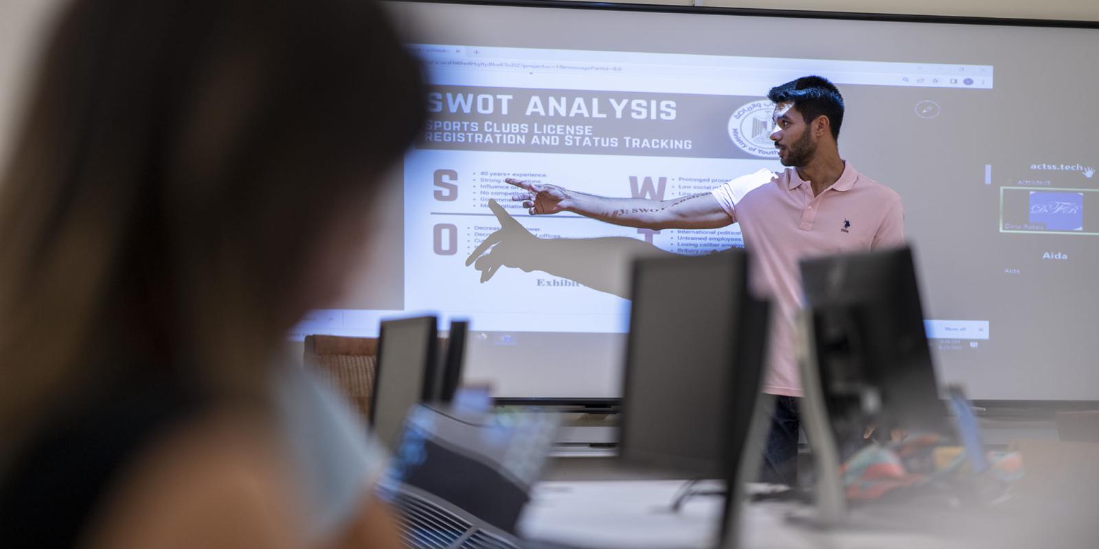 student in class presenting in front of other students on white board