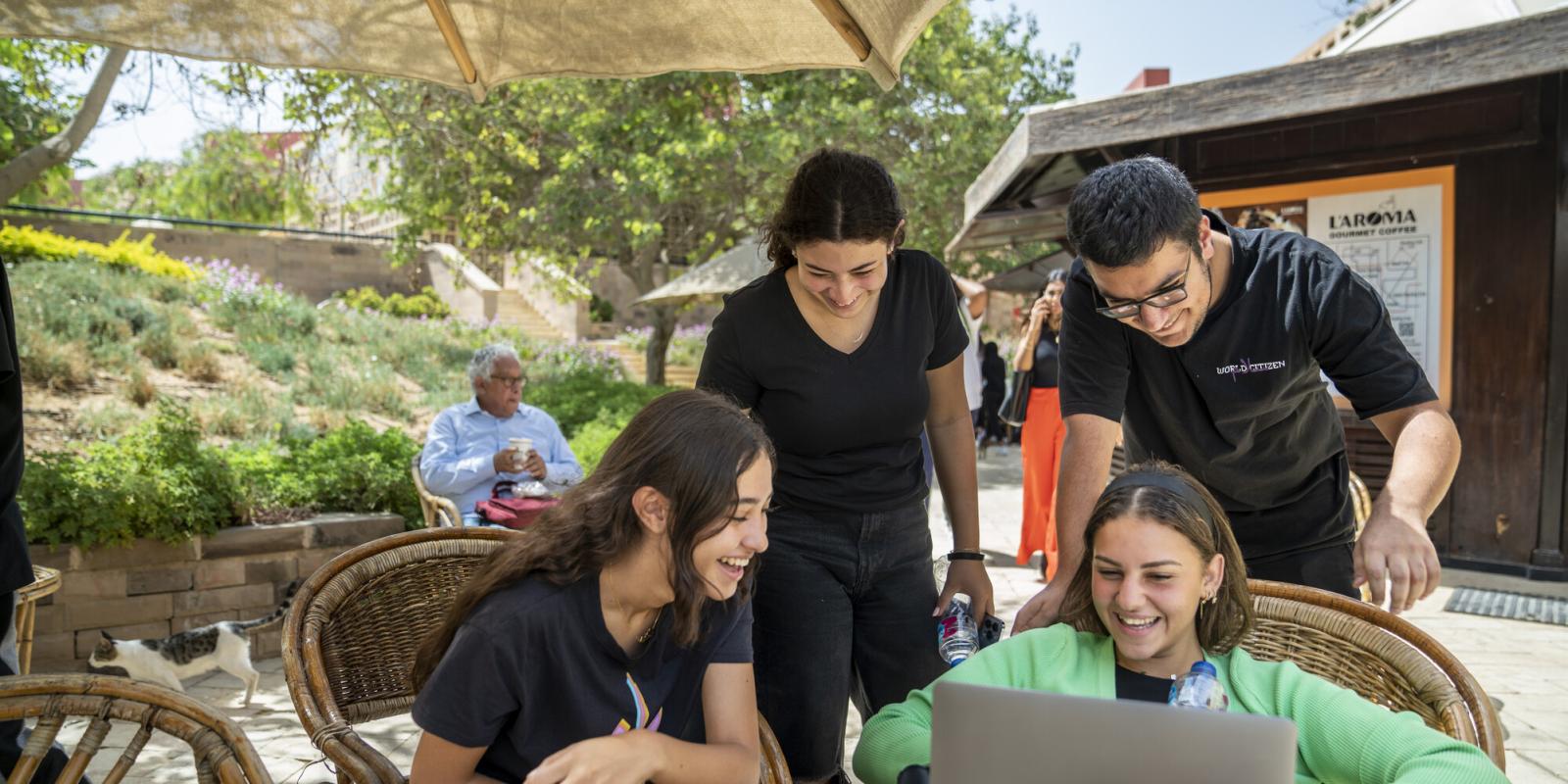 students working in garden on laptop on project and smiling