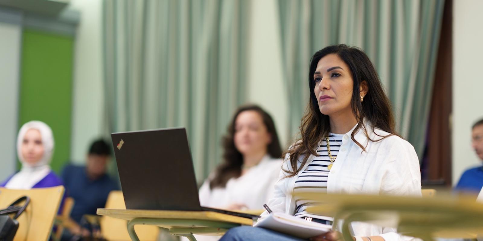 A student sits in a classroom with a laptop and notebook.