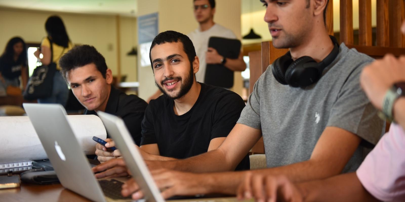 A group of students sit together using laptops while collaborating on work in a study space.